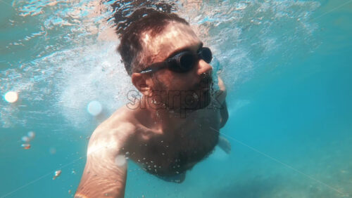 Video - Man in swimming goggles under the water and holding camera, Aegean sea. Slow motion, underwater shooting. Greece