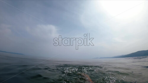 Video - A man swimming in the dark water of a sea. Cloudy sky. First-person view, slow motion