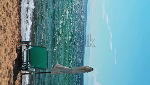 Video - Empty sunbed and closed umbrella on the beach of the Aegean sea, land in the distance in Nikiti, Greece. Vertical shooting