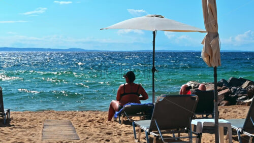 Video - NIKITI, GREECE - OCTOBER 5, 2020: Beach on Aegean sea coast with umbrellas and sunbeds, resting couple, rocks near the water