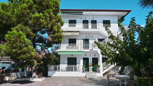 Video - NIKITI, GREECE - OCTOBER 8, 2020: A residential building with three floors, terrace and stairs, multiple greenery around it, road with parked car