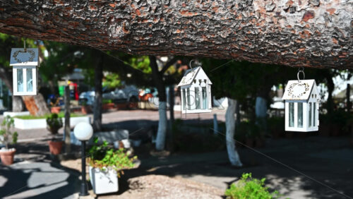 Video - Swaying in the wind cases for candles suspended by a tree branch, garden and road on the background in Nikiti, Greece