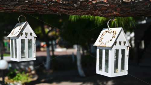 Video - Swaying in the wind cases for candles suspended by a tree branch, garden and road on the background in Nikiti, Greece