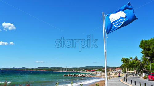 Video - A blue flag with a sign on it near the embankment street, greenery, Aegean sea cost in Nikiti, Greece