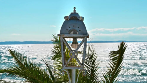 Video - Vintage lamppost painted in white color on the Aegean sea coast, water and plant on the background in Nikiti, Greece