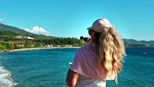 Video - NEOS MARMARAS, GREECE - OCTOBER 8, 2020: Caucasian woman in cap and sunglasses on a viewpoint at Aegean sea coast of Greece taking photos with phone