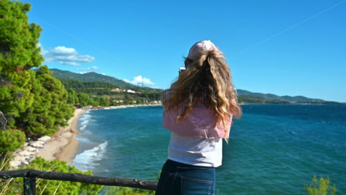 Video - NEOS MARMARAS, GREECE - OCTOBER 8, 2020: Caucasian woman in cap and sunglasses on a viewpoint at Aegean sea coast of Greece taking photos with phone