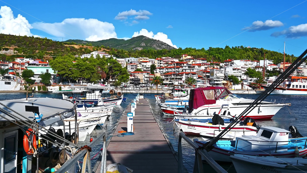 Video - NEOS MARMARAS, GREECE - OCTOBER 8, 2020: Aegean sea port with multiple moored yachts and boats, wooden pier, town located on a hill with greenery, clear weather