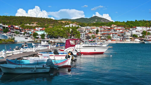 Video - NEOS MARMARAS, GREECE - OCTOBER 8, 2020: Aegean sea port with multiple moored yachts and boats, wooden pier, town located on a hill with greenery, clear weather. Slow motion