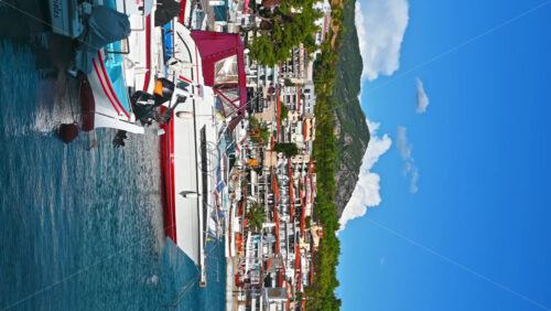 Video - NEOS MARMARAS, GREECE - OCTOBER 8, 2020: Aegean sea port with multiple moored yachts and boats, wooden pier, town located on a hill with greenery, clear weather. Slow motion, vertical shooting