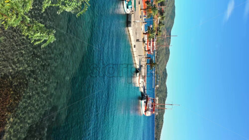 Video - NEOS MARMARAS, GREECE - OCTOBER 8, 2020: Wide pier with few palms on it, three moored sailboats , green hill on the background. Slow motion, vertical shooting