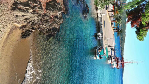 Video - NEOS MARMARAS, GREECE - OCTOBER 8, 2020: Wide pier with few palms on it, moored sailboats , green hill on the background. Slow motion, vertical shooting