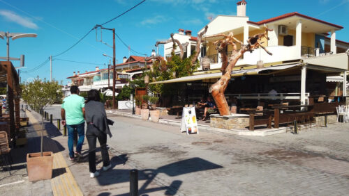 Video - NIKITI, GREECE - OCTOBER 8, 2020: Embankment street of the town located on the Aegean sea coast. Walking and resting people. Rows of buildings and establishments. Slow motion