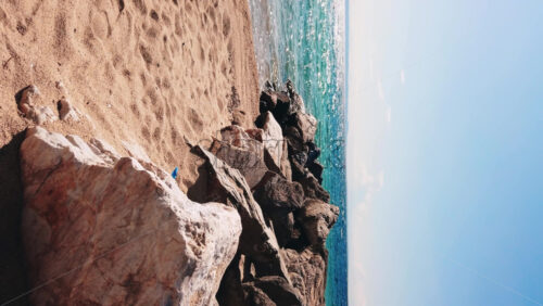 Video - Beach on Aegean sea coast with rocks leading to the water, land in the distance in Nikiti, Greece. Slow motion, vertical shooting