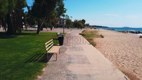 Video - NIKITI, GREECE - OCTOBER 8, 2020: Embankment street near the Aegean sea coast, a lot of greenery, palms and grass, lampposts, gazebo with benches, road. Slow motion
