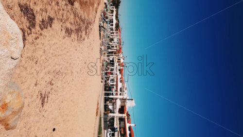 Video - NIKITI, GREECE - OCTOBER 8, 2020: Beach on Aegean sea coast with closed umbrellas and sunbeds, rocks in the water, embankment street, rows of buildings. Slow motion, vertical shooting