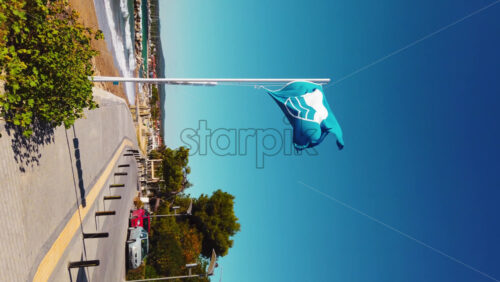 Video - NIKITI, GREECE - OCTOBER 8, 2020: A blue flag with a sign on it near the embankment street, greenery, Aegean sea coast. Vertical shooting, slow motion