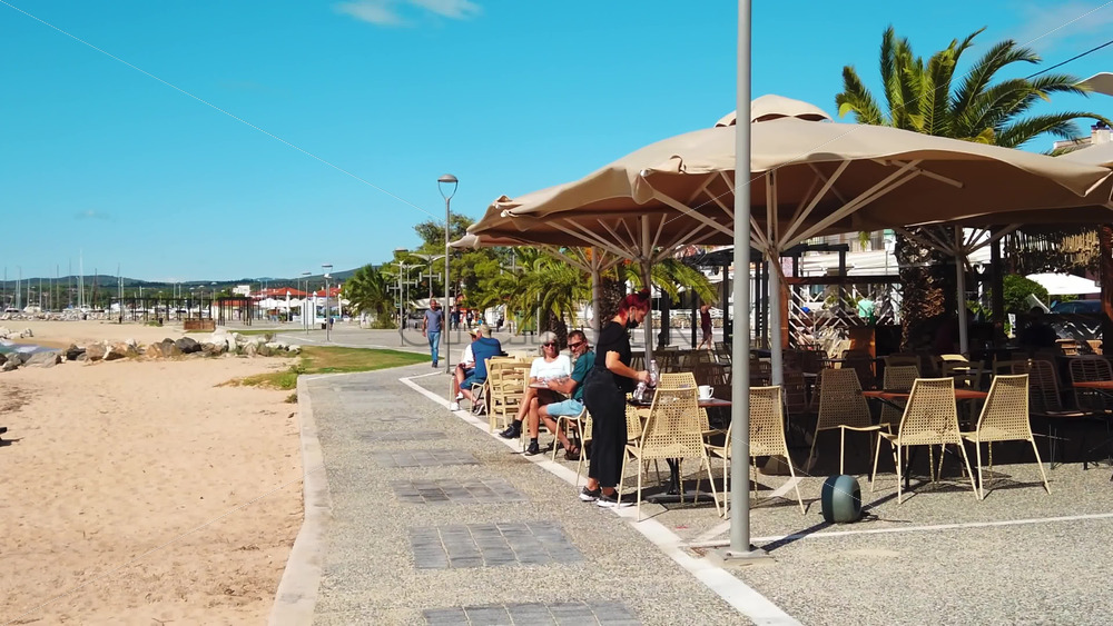 Video - NIKITI, GREECE - OCTOBER 8, 2020: Embankment street of the town located on the Aegean sea coast. Walking waitress and resting people. Rows of buildings, beach. Slow motion