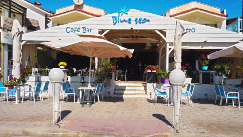 Video - NIKITI, GREECE - OCTOBER 8, 2020: Blue sea cafe bar on the pedestrian street of the town with seats and greenery on the terrace. Slow motion