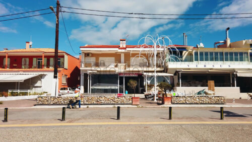 Video - NIKITI, GREECE - OCTOBER 8, 2020: Embankment street of the town located on the Aegean sea coast. Walking woman. Rows of buildings and establishments. Slow motion