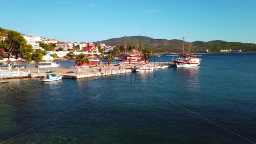 Video - NEOS MARMARAS, GREECE - OCTOBER 8, 2020: Wide pier with few palms on it, three moored sailboats, green hill and town on the background. Slow motion