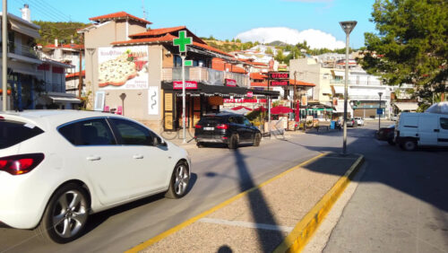 Video - NEOS MARMARAS, GREECE - OCTOBER 8, 2020: Street of the town with caffee, greenery, residentail buildings, moving and parked cars. Slow motion