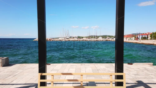 Video - View of sea port with moored yachts, Aegean sea, view from a gazebo on a pier with black metal posts and a bench in Nikiti, Greece. Slow motion