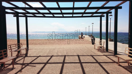 Video - NIKITI, GREECE - OCTOBER 8, 2020: A gazebo on a pier with black metal posts and a benches, Aegean sea. Slow motion