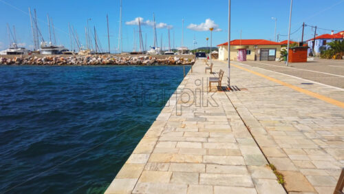 Video - NIKITI, GREECE - OCTOBER 8, 2020: View of sea port with moored yachts, Aegean sea, view from a pier with a bench and lampposts. Slow motion