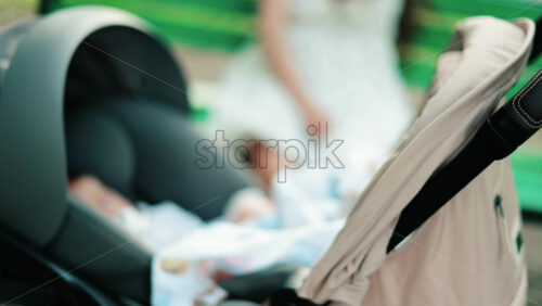 A baby resting in a stroller while a woman sits on a green bench in the background - Starpik Stock