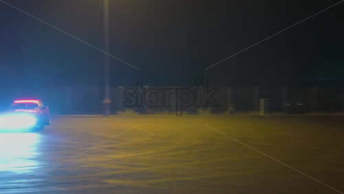 A fast sports car performing a drift in an open lot illuminated by bright streetlights on a rainy night - Starpik Stock
