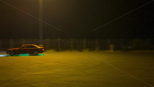 A fast sports car performing a drift in an open lot illuminated by bright streetlights on a rainy night - Starpik Stock