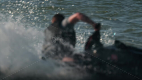 A man in a black life vest riding a black jet ski at high speed across a calm body of water - Starpik Stock