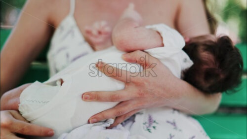 A mother siting on a bench in the park, breastfeeding her baby while enjoying a quiet, peaceful moment in nature. - Starpik Stock