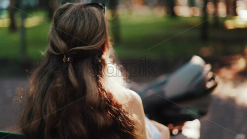 A mother with long wavy hair siting on a bench, breastfeeding her baby in a peaceful park, next to a modern baby stroller - Starpik Stock