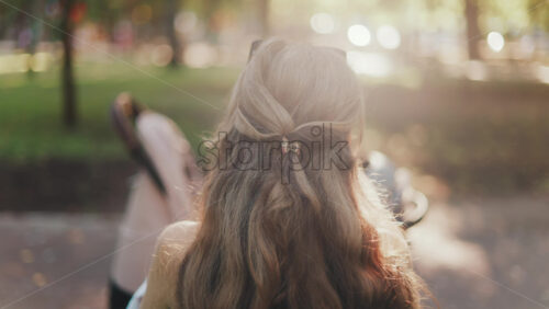 A mother with long wavy hair siting on a bench, breastfeeding her baby in a peaceful park, next to a modern baby stroller - Starpik Stock
