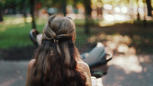 A mother with long wavy hair siting on a bench, breastfeeding her baby in a peaceful park, next to a modern baby stroller - Starpik Stock