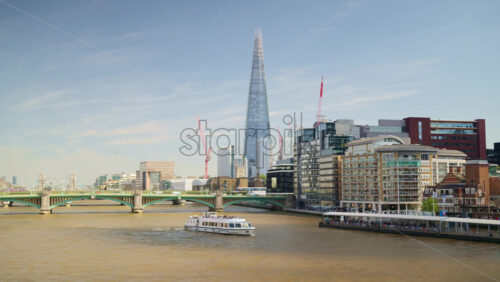 A scenic view of London’s iconic skyline featuring The Shard and Tower Bridge with a tour boat sailing along the River Thames on a sunny day, London, England - Starpik Stock