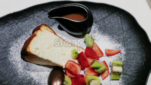 A slice of cheesecake served with fresh strawberries and kiwi, garnished with powdered sugar on a plate at a restaurant - Starpik Stock