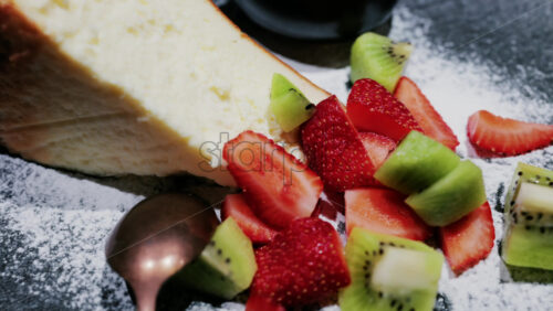 A slice of cheesecake served with fresh strawberries and kiwi, garnished with powdered sugar on a plate at a restaurant - Starpik Stock