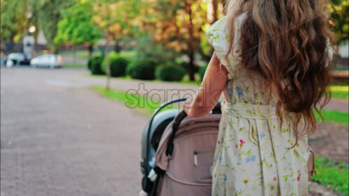 A woman in a floral dress pushing a baby stroller along a park path - Starpik Stock
