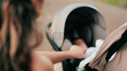 A woman with long curly hair holding a stroller while sitting on a park bench surrounded by greenery - Starpik Stock