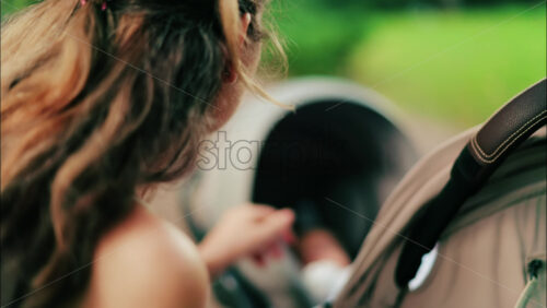 A woman with long curly hair holding a stroller while sitting on a park bench surrounded by greenery - Starpik Stock
