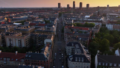 Aerial drone view down a long Copenhagen avenue lined with historic apartments and rooftops, with modern towers in the distance in Denmark - Starpik Stock