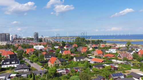 Aerial drone view of Amager residential area with red-roofed houses, and wind turbines in the Oresund Strait in the background in Copenhagen, Denmark - Starpik Stock