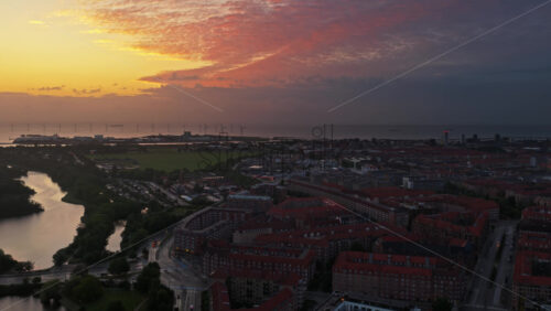 Aerial drone view of Amagerbro in Copenhagen, Denmark at sunset with glowing skies, red rooftops, and wind turbines along the coastline - Starpik Stock