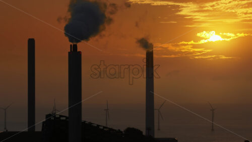 Aerial drone view of CopenHill chimneys with smoke rising against the orange sunrise sky in Copenhagen, Denmark - Starpik Stock