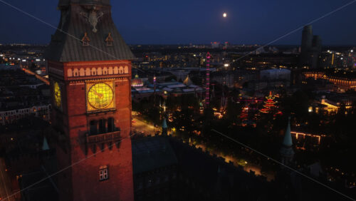 Aerial drone view of Copenhagen City Hall’s illuminated clock tower at night, highlighting the historic details and glowing clock face - Starpik Stock