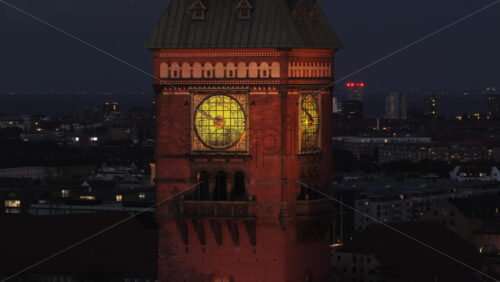 Aerial drone view of Copenhagen City Hall’s illuminated clock tower at night, highlighting the historic details and glowing clock face - Starpik Stock