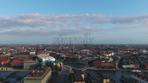 Aerial drone view of Copenhagen, Denmark with historic towers, modern buildings, and red rooftops under a bright morning sky - Starpik Stock